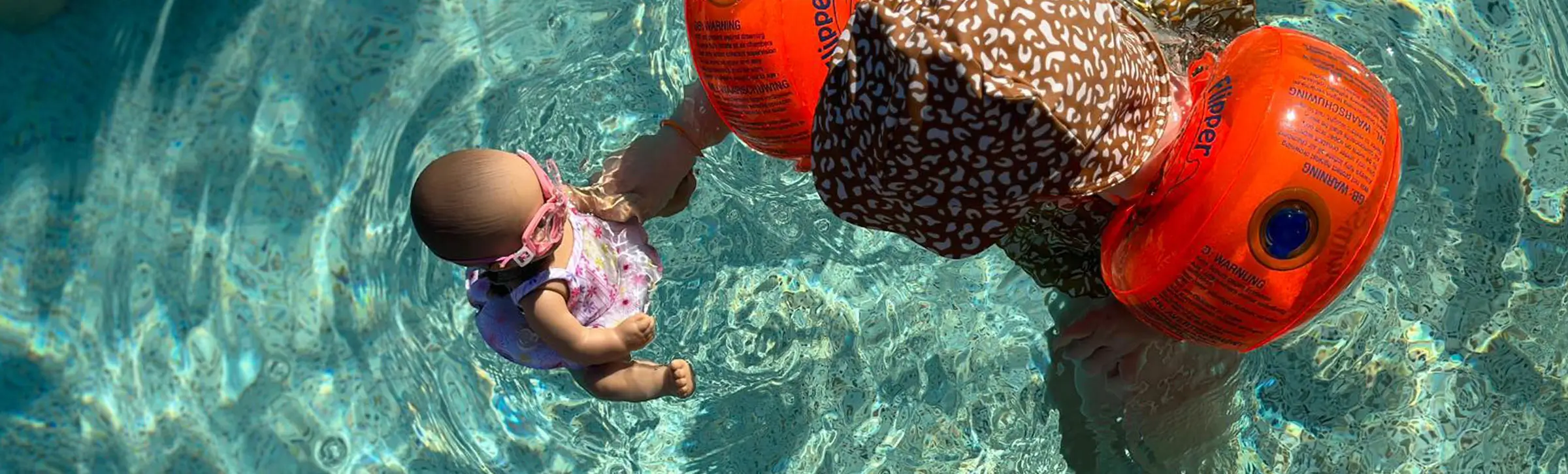 Kind mit Schwimmflügeln spielt im Pool mit 33 cm großer Badepuppe in Schwimmkleidung