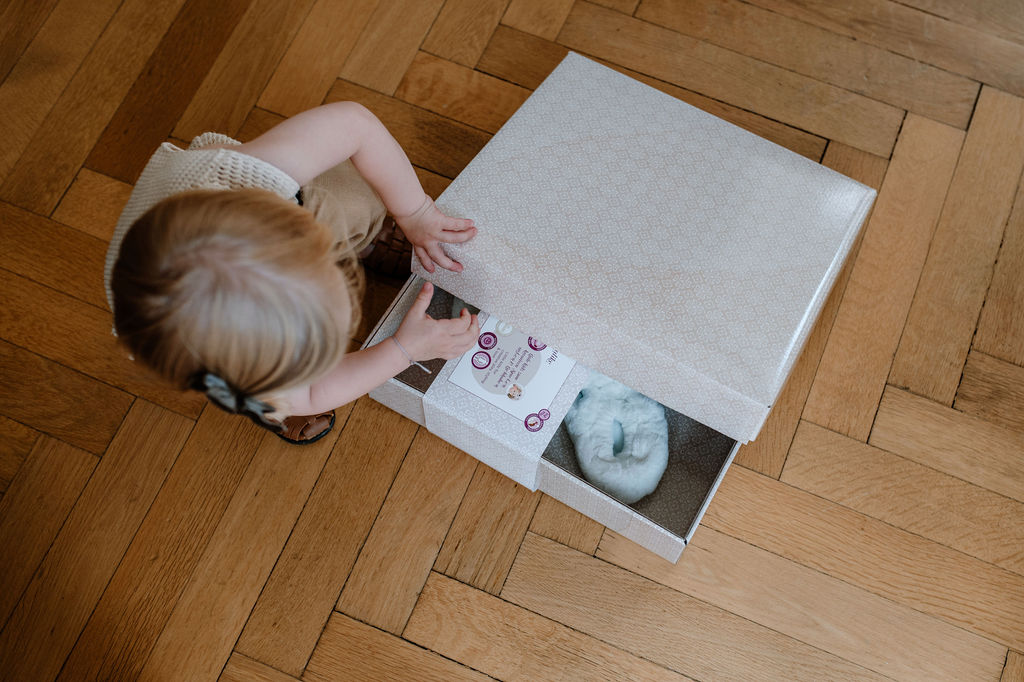 Kind oeffnet Geschenkbox auf Holzboden