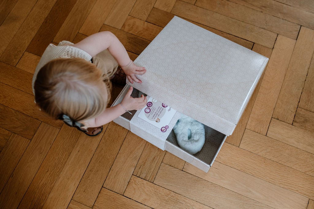 Geschenkbox fuer Kind und Puppe Goetz Kind oeffnet Geschenkbox auf Holzboden