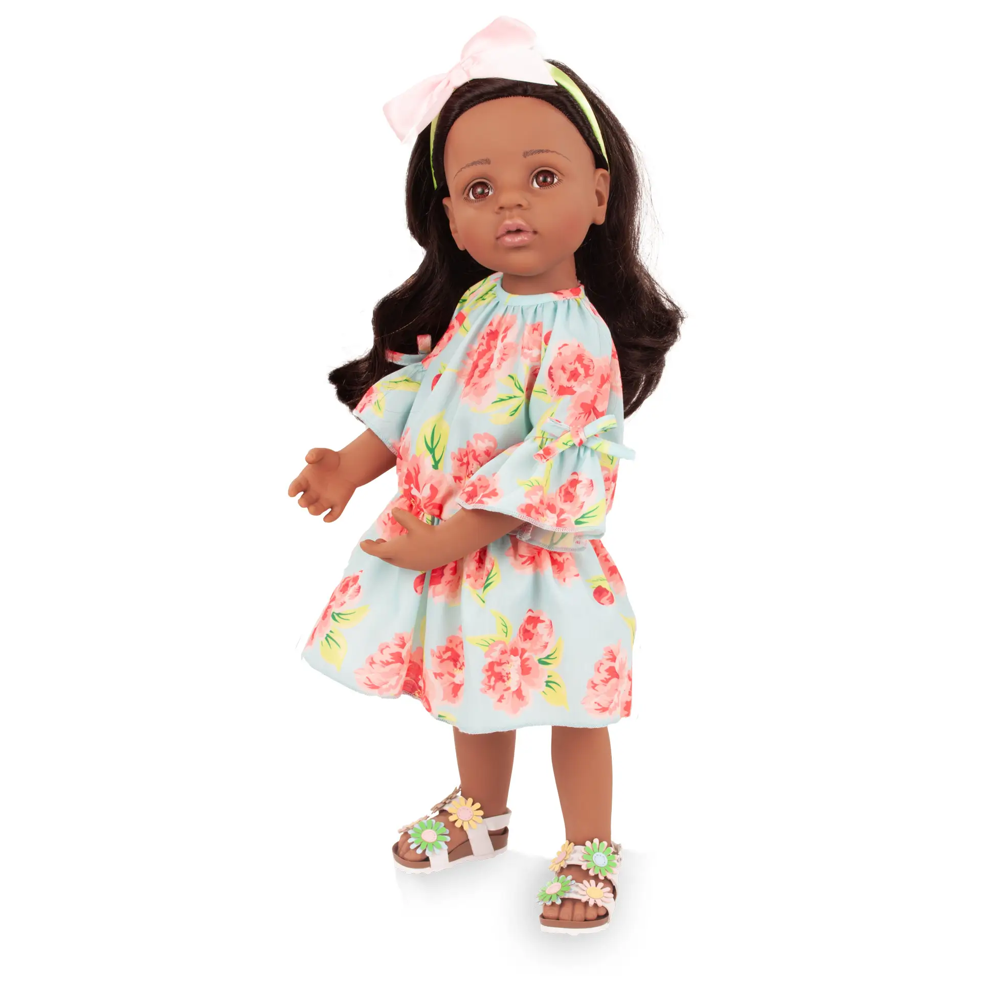 Stehpuppe Gr. 50 cm mit braunem Vinyl, schwarzem Haar und braunen Augen. Sie traegt ein Rosenkleid mit Blumensandalen und einem Schleifen-Haarreif von Goetz