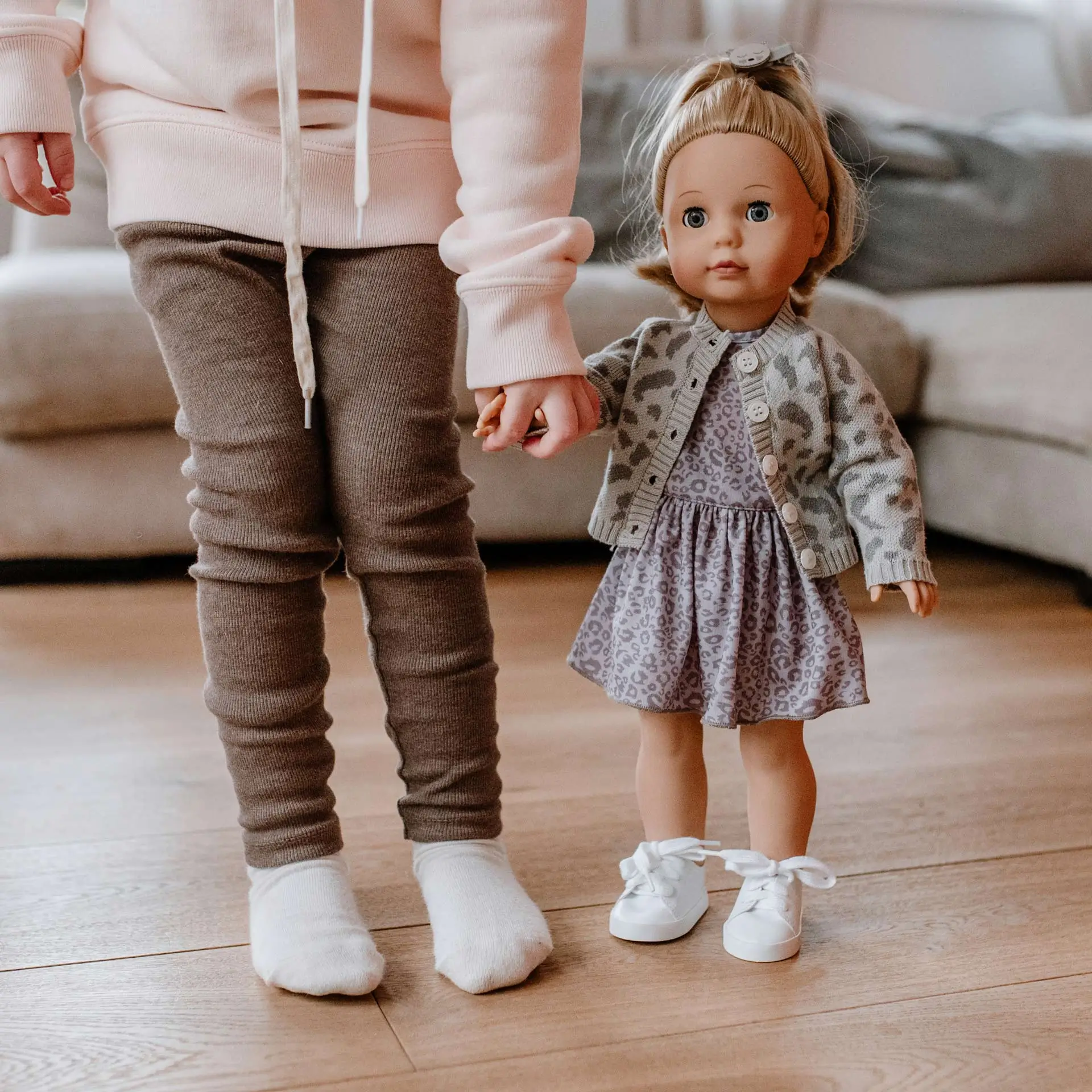 Kind haelt die Hand einer 46 cm grossen Stehpuppe mit blonden Haaren und blauen Schlafaugen im Leo-Kleid