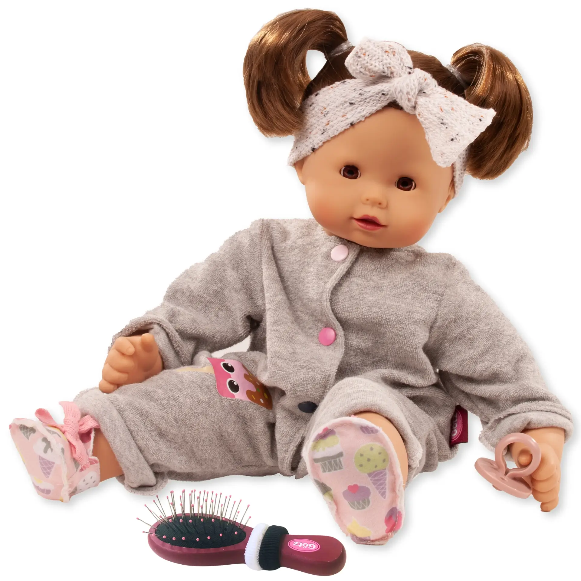 Babypuppe Gr. 42-46 cm in einem grauen Frotteeanzug und einem Strick-Haarband und Stoffschuhen. Sie hat braunes Haar und braune Schlafaugen, dazu einen Schnuller und eine Buerste mit zwei Haargummis von Goetz