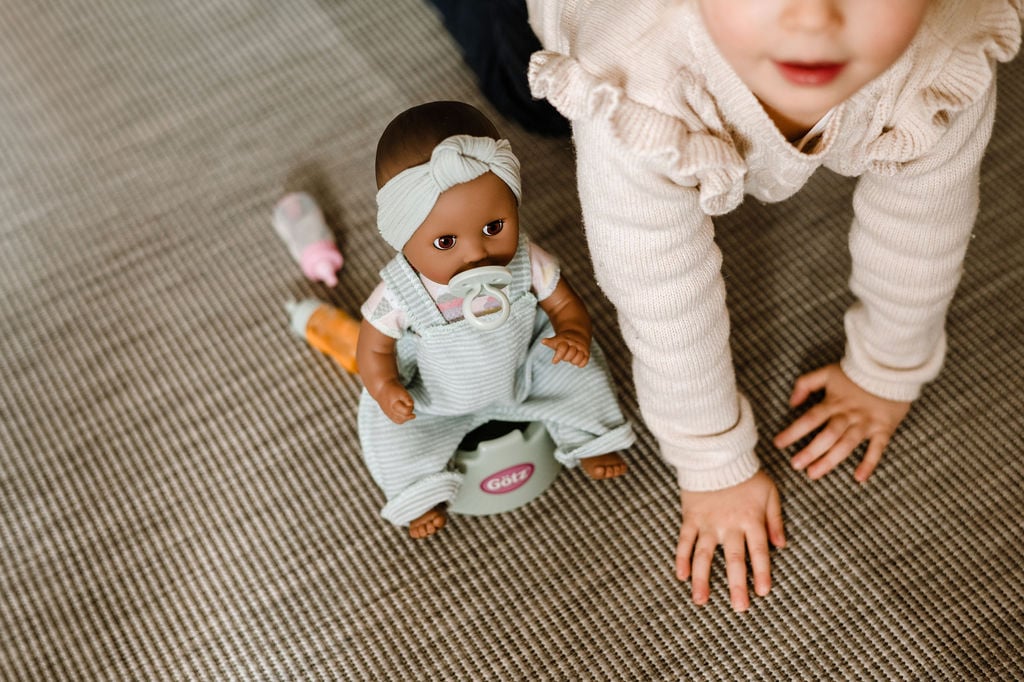 Badespaß im Sommer und Winter mit Goetz Kind spielt mit einer 33 cm grossen dunkelhaeutigen Babypuppe, die auf einem Topf sitzt und einen Schnuller im Mund hat