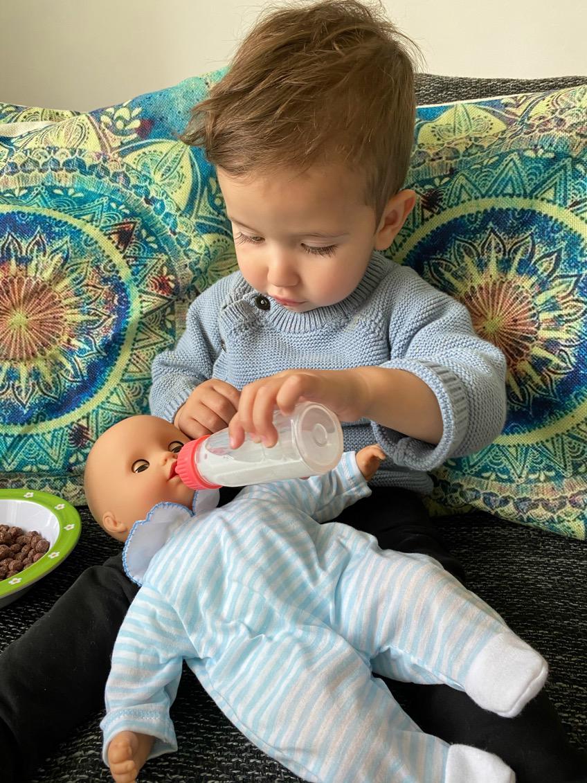 Kind fuettert 33 cm grosse Babypuppe mit Schlafaugen mit einer Milchflasche