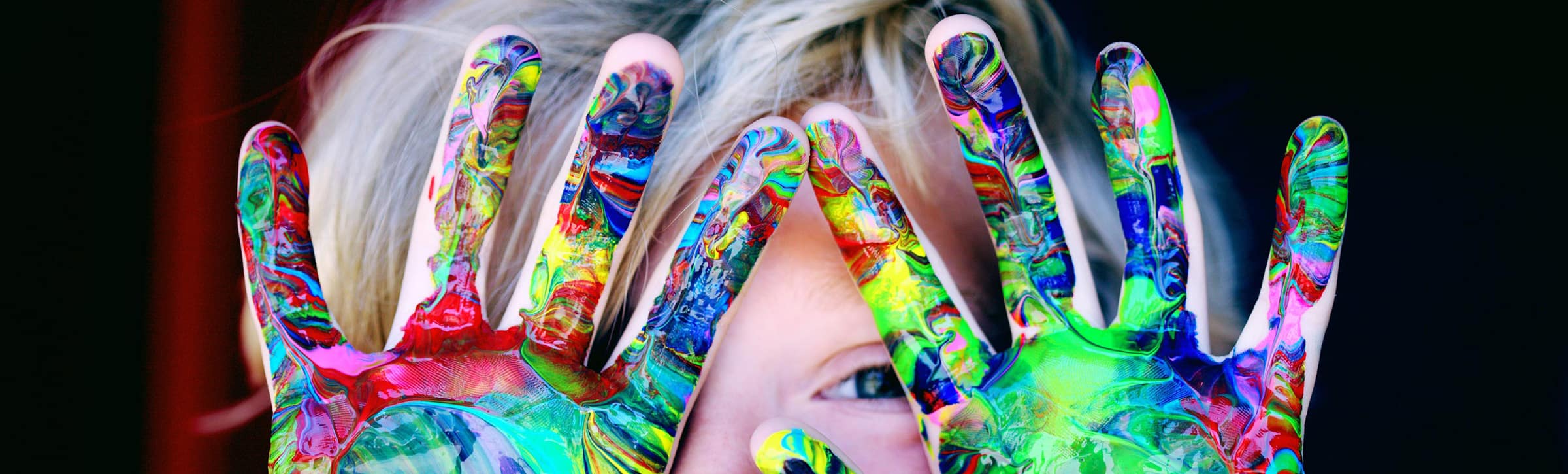 Let your life be colourful Goetz Kind haelt bunt bemalte Haende vor das Gesicht