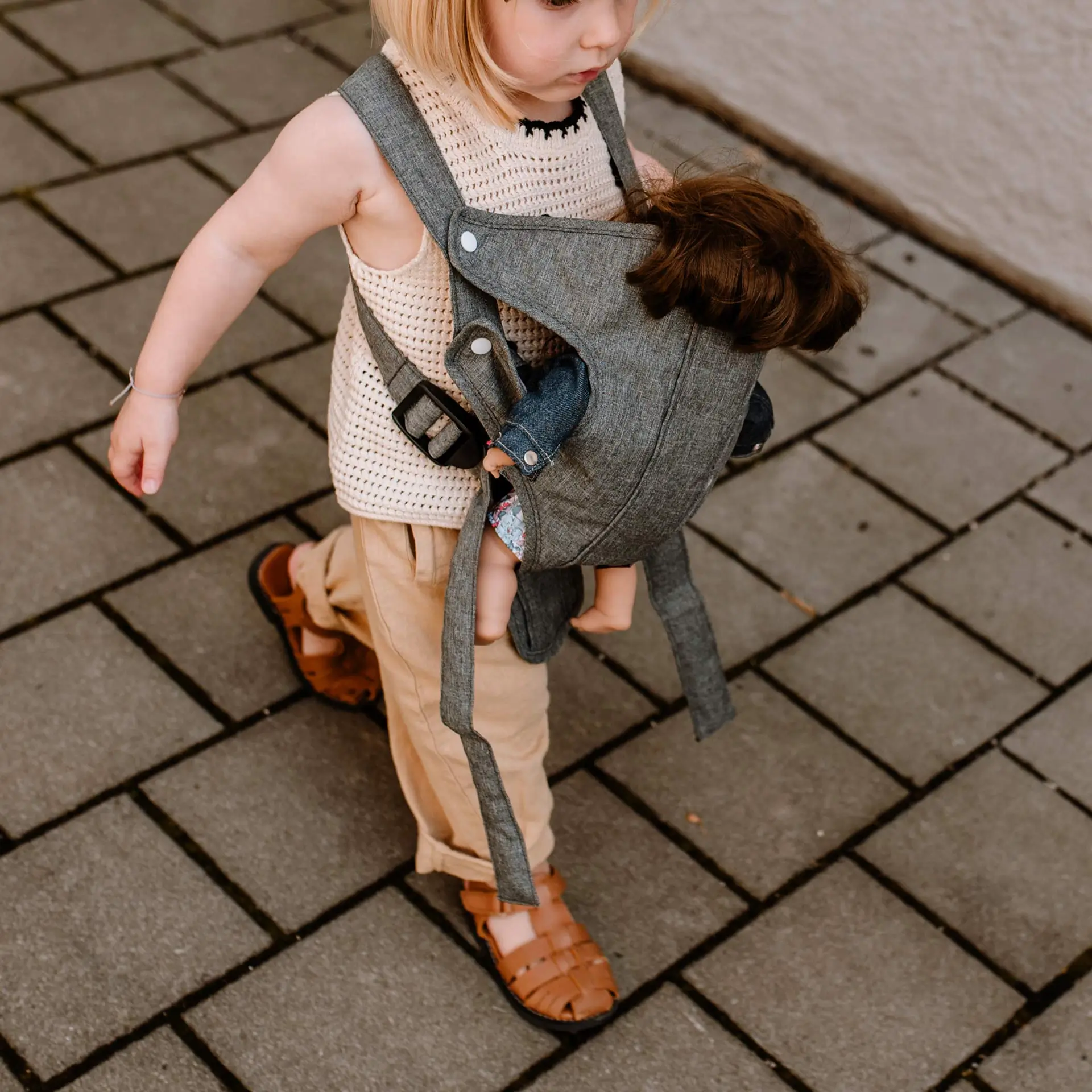 Kind traegt eine Babypuppe in eine  Bauchtrage