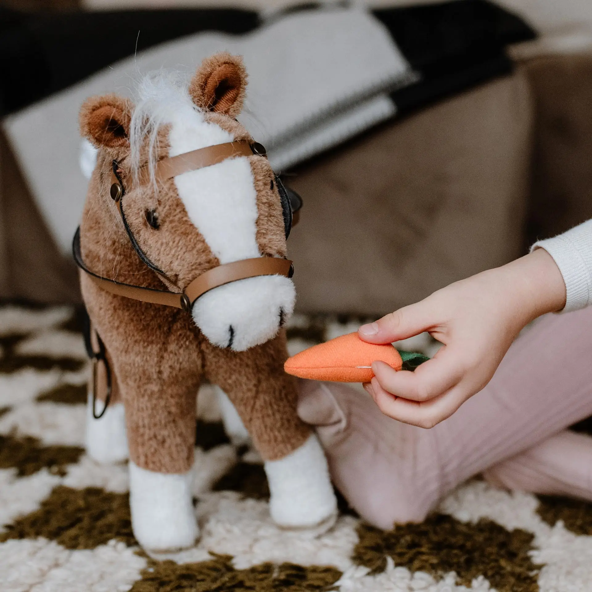 Kind fuettert ein braunes Plueschpferd mit einer Karotte