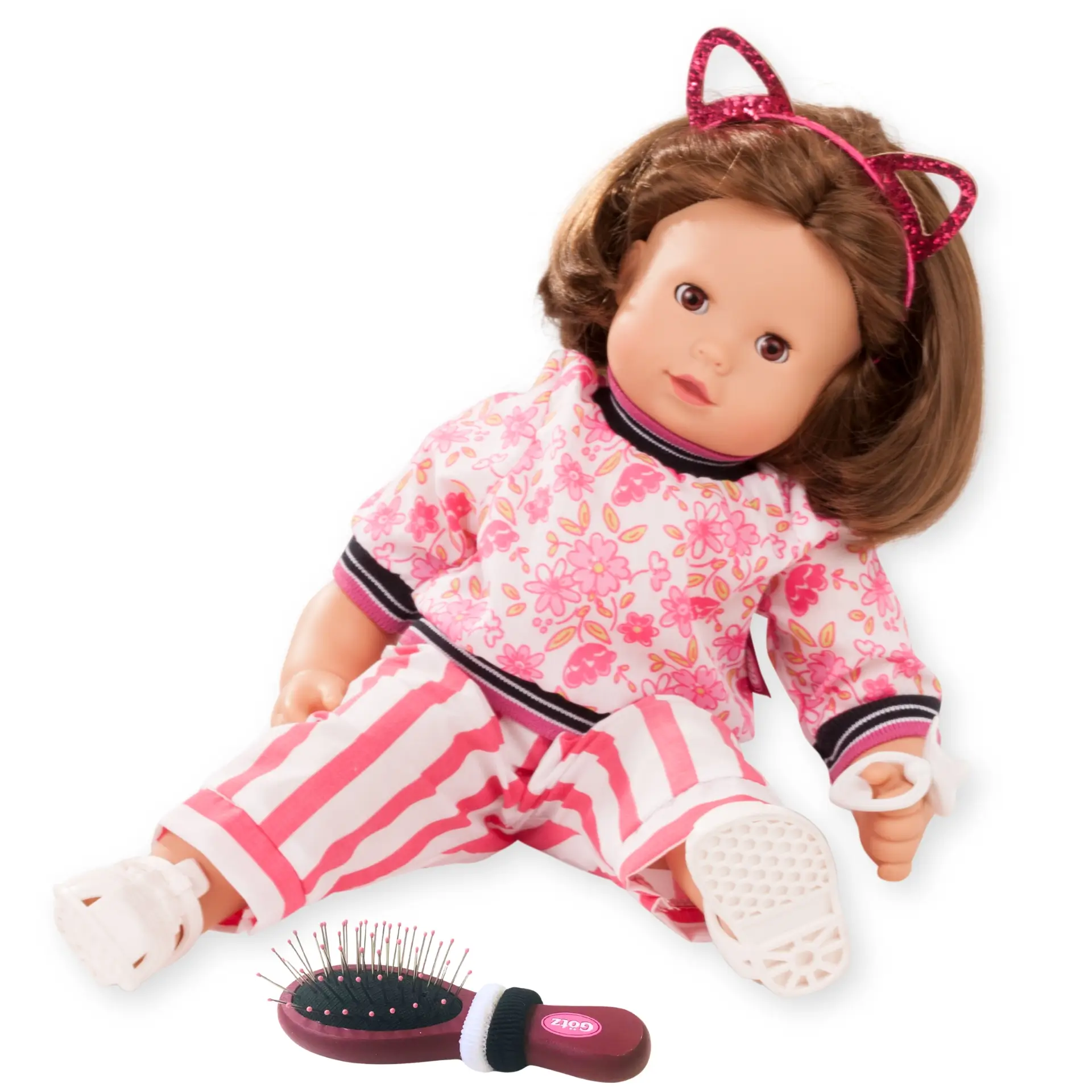 Babypuppe Gr. 42-46 cm mit braunem Haar und braunen Schlafaugen. Sie traegt ein rot-weißes Outfit mit weißen Gummisandalen, einem Katzenohr-Haarreif. Eine Buerste mit zwei Haargummis ist noch dabei und ein Schnuller von Goetz