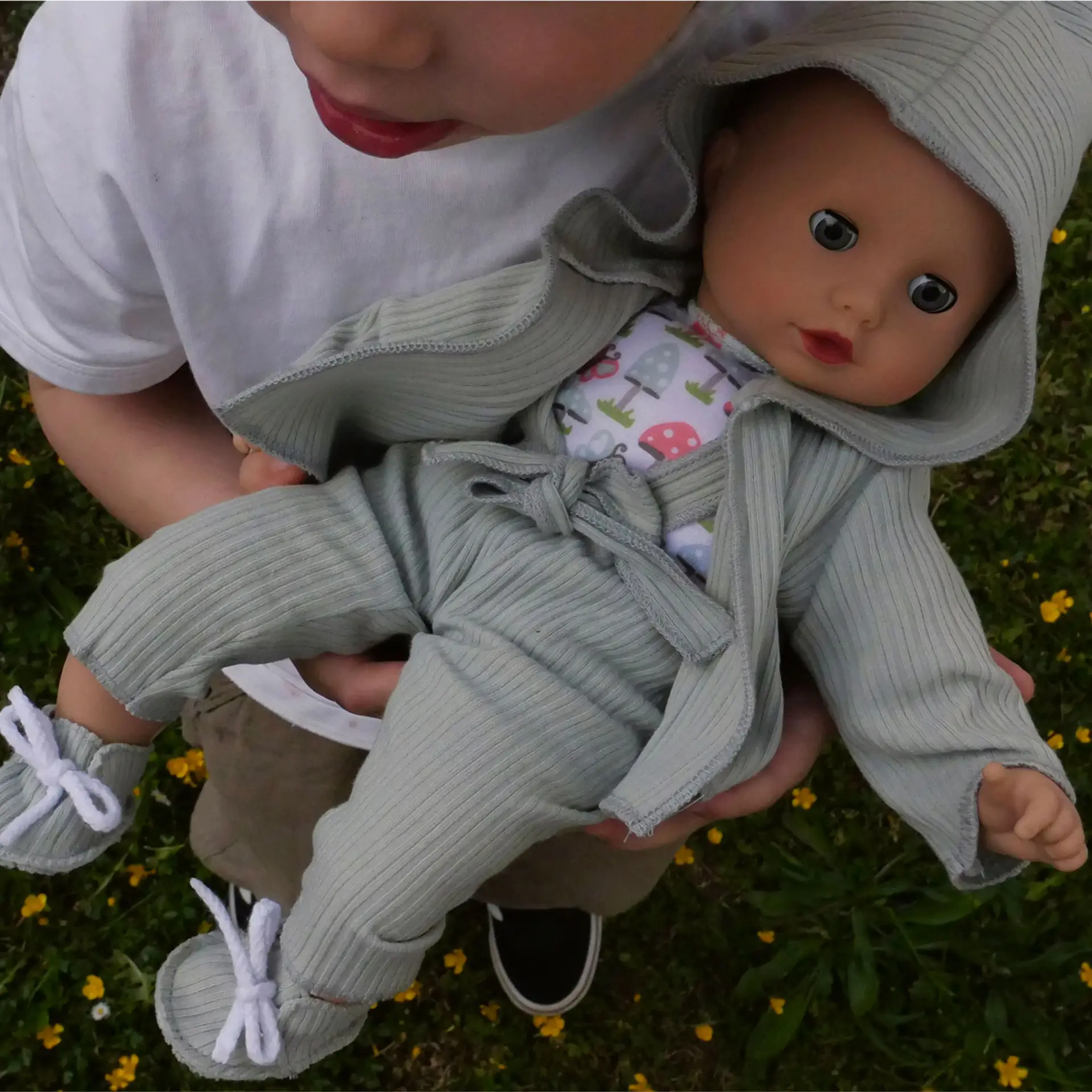 2320553 Muffin Glueckspilz Babypuppe Goetz Kind haelt 33 cm grosse Babypuppe mit blauen Schlafaugen in gruener Latzhose und Kapuzenjacke im Arm