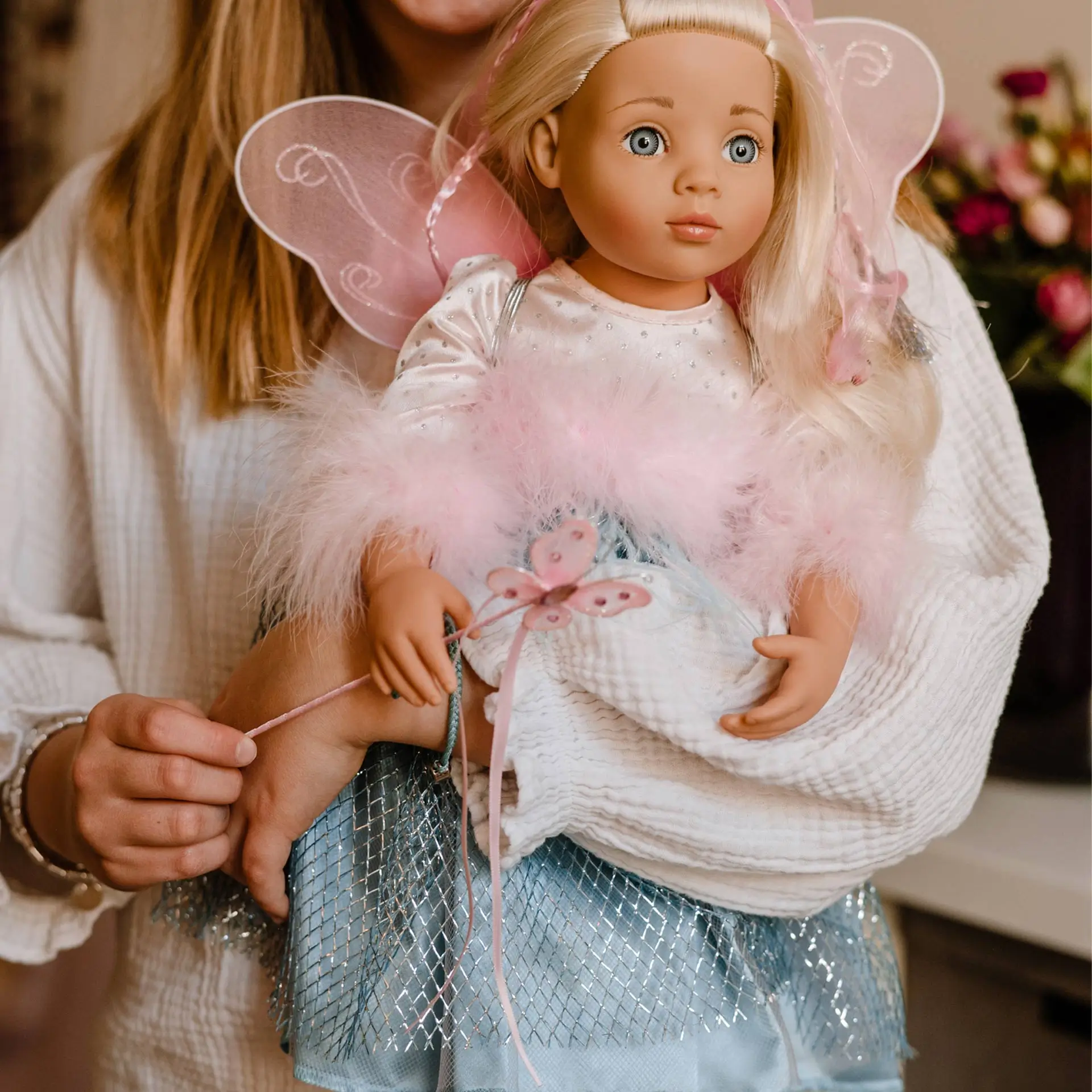 2366086 Happy Kidz Marie Multigelenkstehpuppe Goetz Kind haelt eine 50 cm große Stehpuppe mit blonden Haaren und blauen Augen im Feenkostüm im Arm