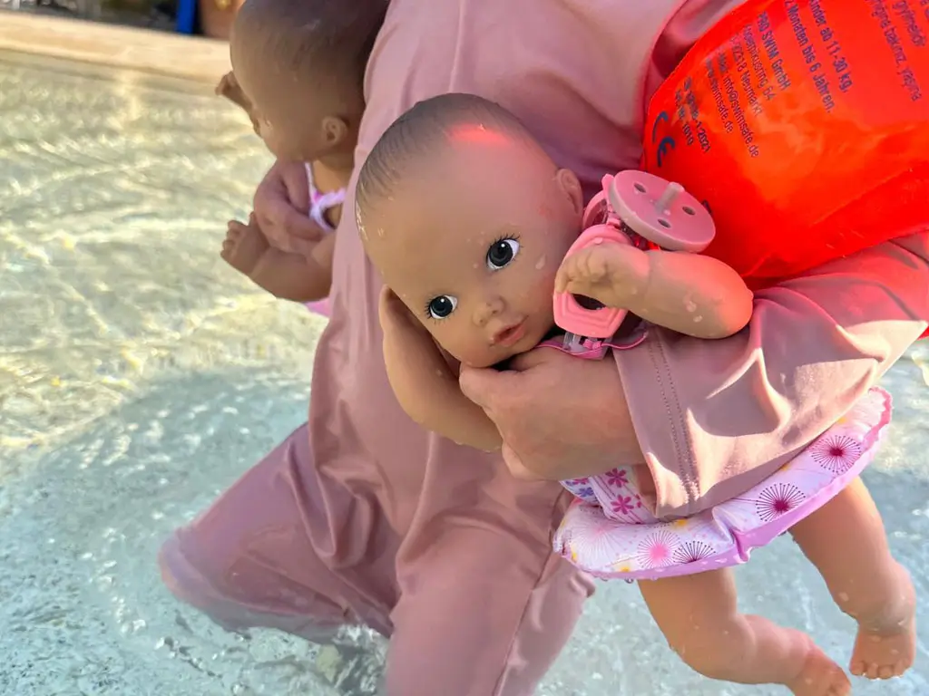 Badepuppe Aquini Goetz Kind hat eine 33 cm grosse Badepuppe mit Badeanzug und Schwimmring im Arm und laeuft durchs Wasser