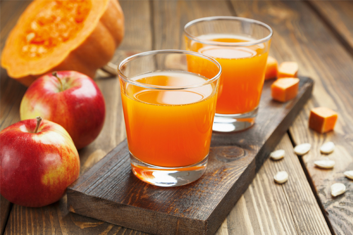 Glas mit Kuerbissaft neben einem Kuerbis und einem Apfel