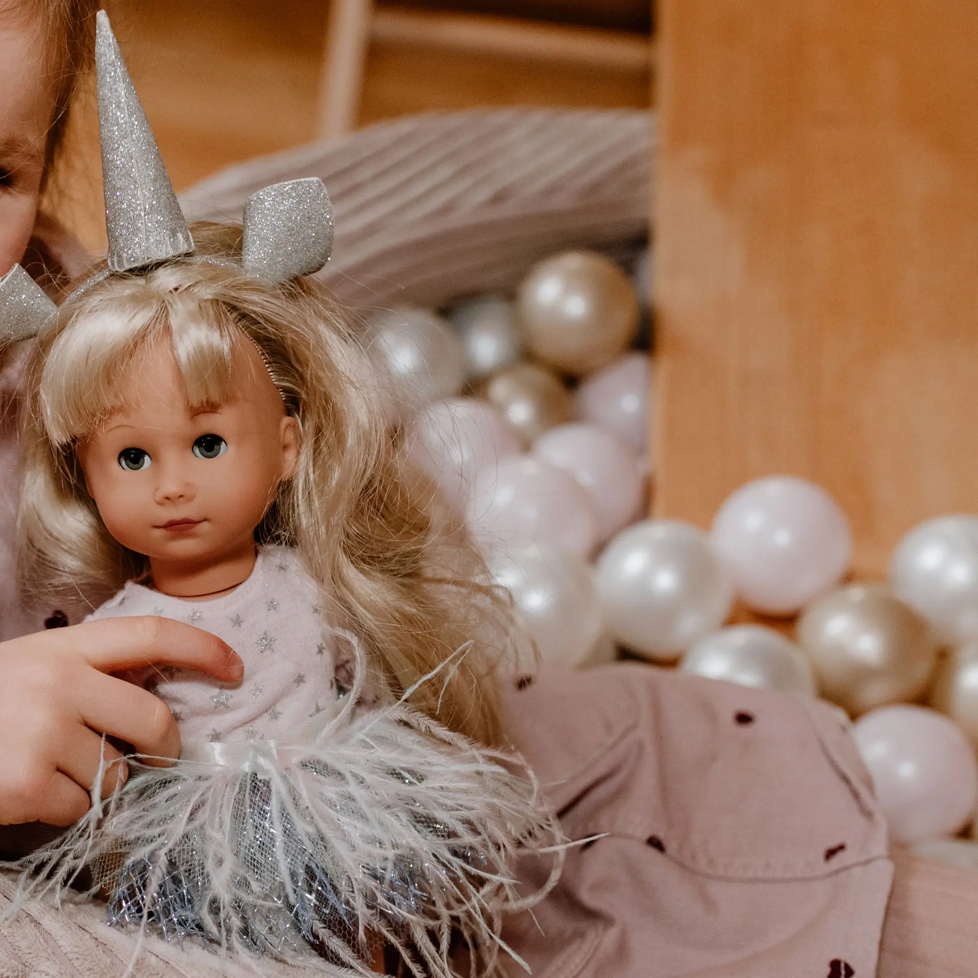 27 cm grosse Stehpuppe mit blonden Haaren im Einhornkostüm sitzt auf dem Schoss eines Kindes